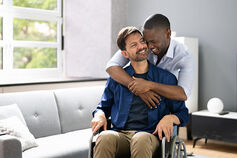 A man in a wheelchair is embraced by another man.